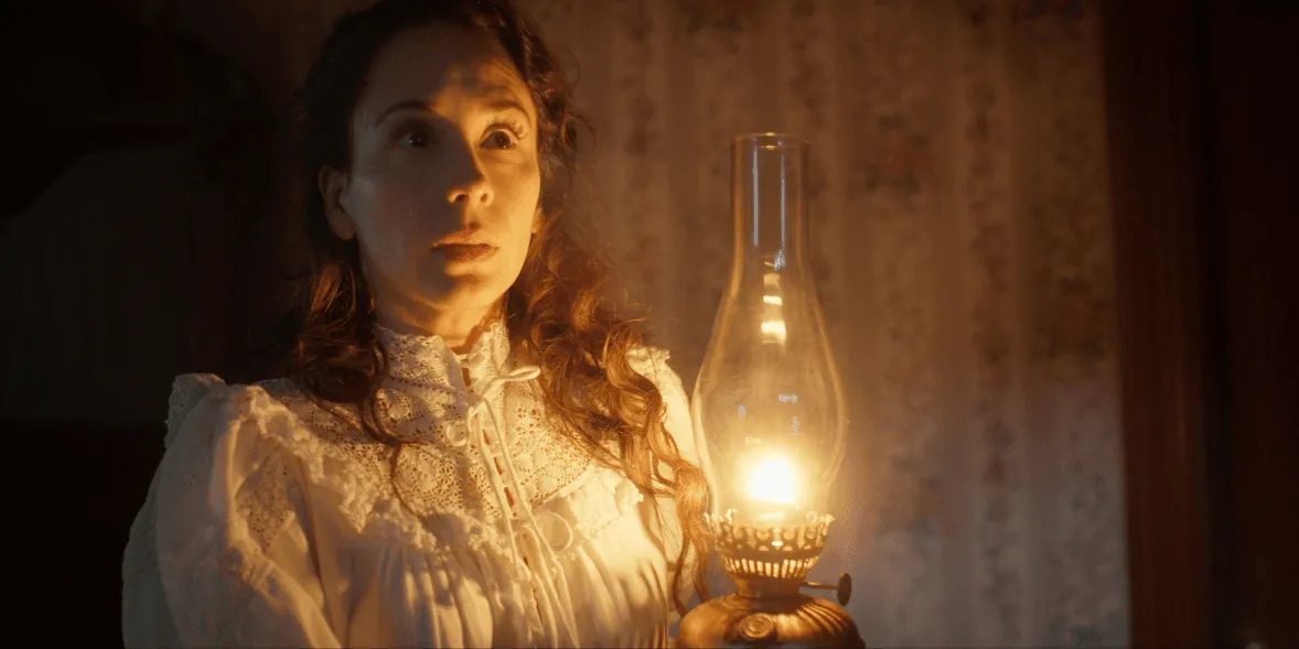 A young woman holds a candle in a dark room.
